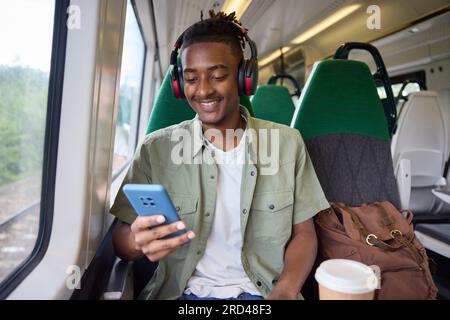 Jeunes hommes se rendant au travail sur le train assis sur le train regardant le téléphone portable pour des informations de voyage ou les médias sociaux Banque D'Images