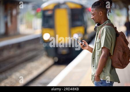 Jeune homme qui se rend au travail sur le train debout sur la plate-forme regardant le téléphone portable à l'arrivée du train Banque D'Images