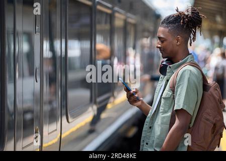 Jeune homme qui se rend au travail sur le train debout sur la plate-forme regardant le téléphone portable à l'arrivée du train Banque D'Images