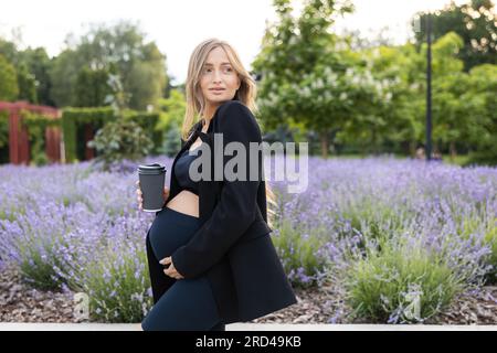 Femme enceinte marchant dans un parc et buvant du café à l'extérieur Banque D'Images