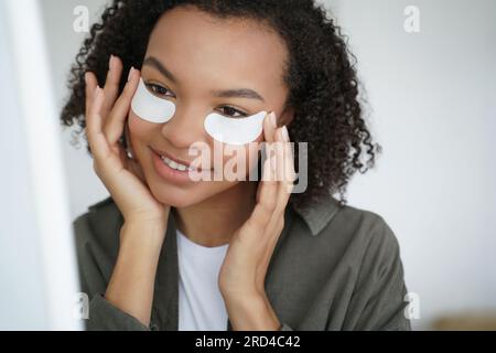 Joyeuse fille afro-américaine utilise des caches pour les yeux pour la peau jeune. Publicité soins de la peau. Banque D'Images