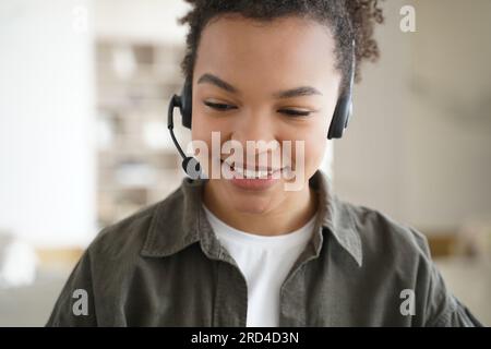 Heureux adolescent de race mixte apprend la langue étrangère en ligne, en utilisant des écouteurs pour l'éducation à distance. Banque D'Images