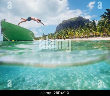 Saut adolescent garçon de bateau en bois plongée avec tuba dans le lagon turquoise propre sur la plage de palmiers le Morne avec le mont le Morne Brabant. Île Maurice. Banque D'Images