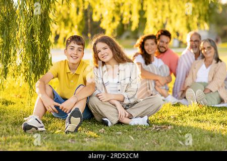 Joyeux adolescent caucasien garçon et fille se détendre avec les parents et les grands-parents, profiter du pique-nique dans le parc Banque D'Images