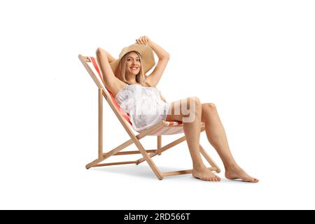 Belle jeune femme dans une robe blanche et chapeau de paille assis sur une chaise de plage isolé sur fond blanc Banque D'Images