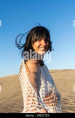 Suivez-moi concept. Une femme souriante aux cheveux longs marchant sur le sable tenant la main de quelqu'un Banque D'Images