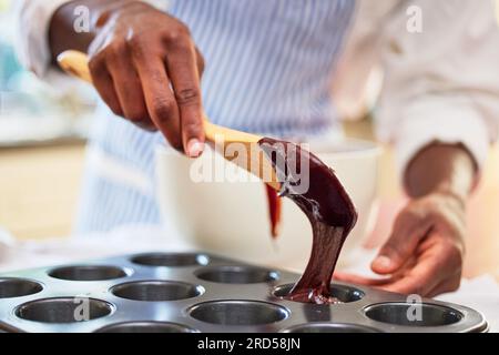 Cupcake, chocolat et les mains d'une personne faisant cuire dans une cuisine et cuisine recette de dessert le matin. Restaurant, homme et chef professionnel Banque D'Images