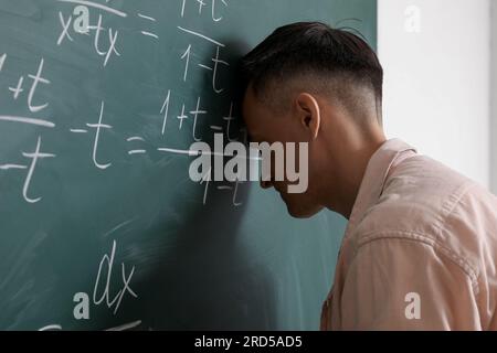 Professeur de maths fatigué près du tableau dans la salle de classe Banque D'Images