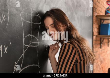 Professeur de mathématiques féminin stressé près du tableau noir dans la salle de classe Banque D'Images