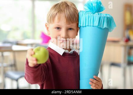 Heureux petit garçon avec cône d'école bleu et pomme fraîche en classe Banque D'Images