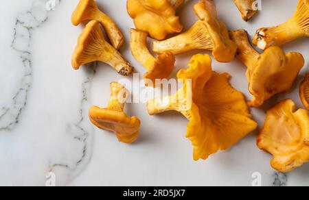Chanterelles de champignons de la forêt orange dans un panier en osier et éparpillées sur une table en bois blanc. Gros plan. Flou d'arrière-plan Banque D'Images