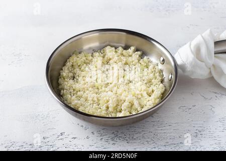 Poêle à frire avec du riz non cuit et des oignons sur un fond bleu clair. Comment faire du risotto maison à la poire et au gorgonzola étape par étape. Banque D'Images