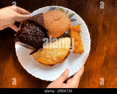 Variété déférente d'affichage de collations sur une assiette une main tient un muffin au chocolat sur fond de bois Banque D'Images