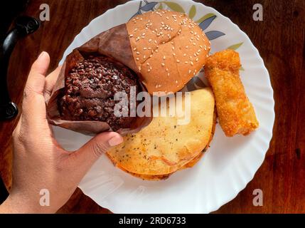 Variété déférente d'affichage de collations sur une assiette une main tient un muffin au chocolat sur fond de bois Banque D'Images