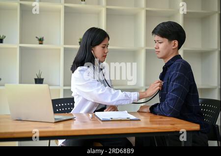 Un médecin asiatique professionnel vérifie et écoute le rythme cardiaque d'un patient avec un stéthoscope pendant le bilan médical à l'hôpital. Banque D'Images