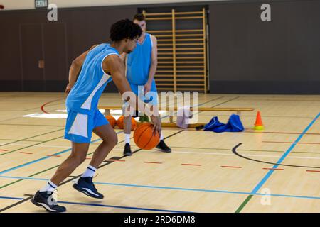 Divers joueurs de basket-ball masculins portant des vêtements de sport bleus et jouant au basket-ball à la salle de gym Banque D'Images