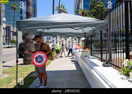 Hollywood, Californie, États-Unis 18 juillet 2023. Un bel homme noir tenant un bouclier Captain America qui dit : « nous pouvons faire ça toute la journée », se réfugie sous une tente devant la ligne de piquetage. Les acteurs hollywoodiens rejoignent Writers (qui frappent depuis deux mois) le deuxième jour de la grève de Screen Actors Guild, devant le siège de Netflix et Sunset Studios à Hollywood, en Californie. Les esprits étaient élevés malgré l'avertissement de chaleur extrême en cours à Los Angeles, et les tempéraments chauds sur la perception de la cupidité de l'entreprise et l'échec des cadres de cinéma et de télévision à répondre à leurs besoins. Banque D'Images