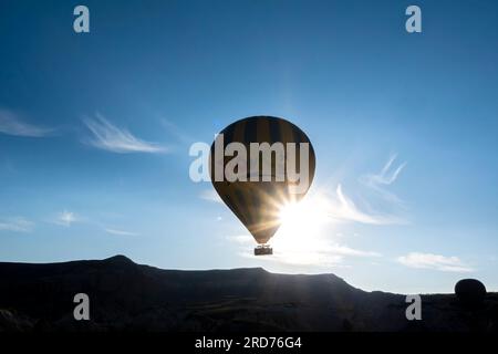 Montgolfière face au soleil levant, silhouette de montgolfière contre la montagne rocheuse Cappadoce Turquie. Soleil brillant à travers le ballon d'air. Banque D'Images