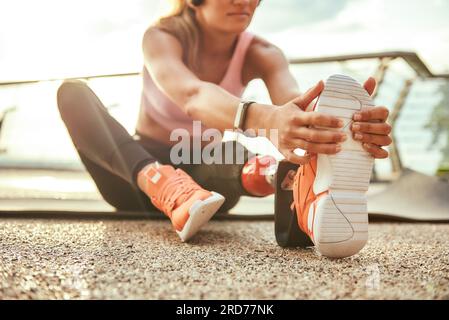 Exercices d'étirement. Photo recadrée de jeune belle femme dans un casque avec prothèse de jambe écoutant de la musique et étirant sa jambe en étant assis dessus Banque D'Images