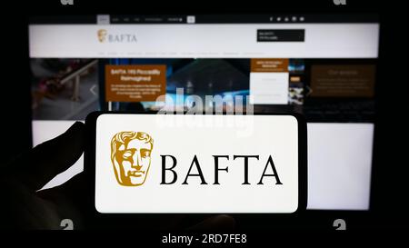 Personne tenant un smartphone avec le logo des British Academy film Awards (BAFTA) sur l'écran devant le site Web. Concentrez-vous sur l'affichage du téléphone. Banque D'Images