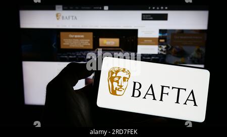 Personne tenant un téléphone portable avec le logo des British Academy film Awards (BAFTA) sur l'écran devant la page Web. Concentrez-vous sur l'affichage du téléphone. Banque D'Images