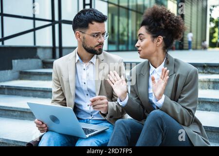 Bel homme et belle femme travaillant sur ordinateur portable sans fil près du centre de bureau. Deux collègues d'affaires assis dans les escaliers et travaillant à distance Banque D'Images