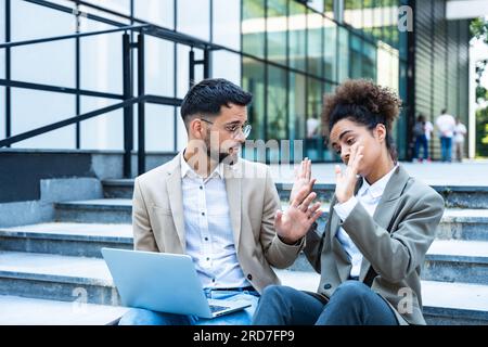 Bel homme et belle femme travaillant sur ordinateur portable sans fil près du centre de bureau. Deux collègues d'affaires assis dans les escaliers et travaillant à distance Banque D'Images