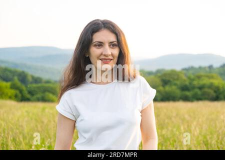 Portrait d'une belle femme brune qui regarde pensivement sur le côté et sourit tout en se tenant dans un champ en été. Banque D'Images