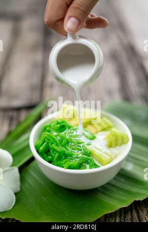 Gros plan de Lod Chong appétissant étant versé avec du lait de coco frais sur feuille de banane sur fond de bois. Banque D'Images