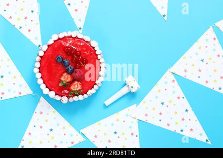 Gâteau cadeau festif sur fond bleu, vue de dessus, plat. Gâteau d'anniversaire, cornes festives et drapeaux des fêtes. espace de copie Banque D'Images