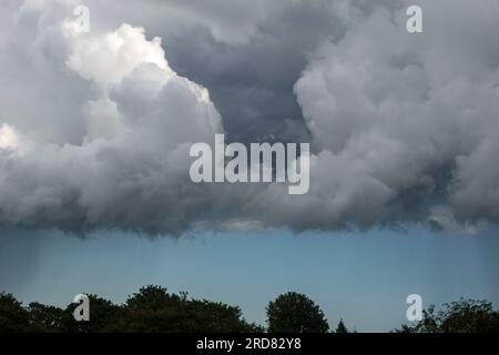 Couches menaçantes de nuages formant une ligne droite avec une bande de ciel clair montrant une tache plus sombre de pluie. Banque D'Images