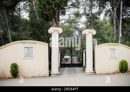 Un double ensemble de portes en fer forgé montées entre des colonnes classiques avec des chapiteaux ioniques placés dans le mur de la propriété avec de nombreux avis de sécurité, Céphalonie. Banque D'Images