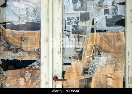 Une vitrine de magasin vide et une porte couverte à l'intérieur par un montage de journaux collés au hasard, Céphalonie, Grèce Banque D'Images