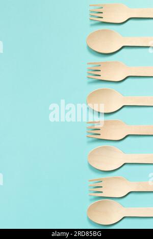 Fourchettes et cuillères jetables en bois sur un fond bleu, vue de dessus. Ustensiles de cuisine jetables respectueux de l'environnement, espace de copie. Pose à plat. Cuillères et fourchettes la Banque D'Images