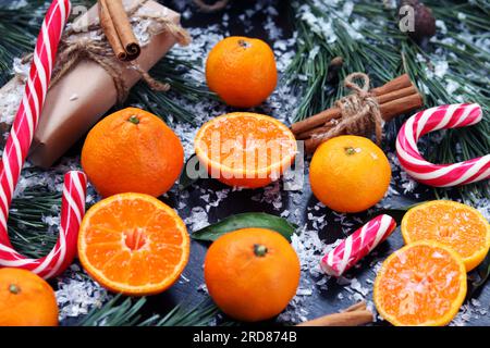 Fond de Noël avec des mandarines, des bonbons, des cadeaux et des branches de sapin sur une table sombre avec de la fausse neige, mise au point sélective. Composition du nouvel an Banque D'Images