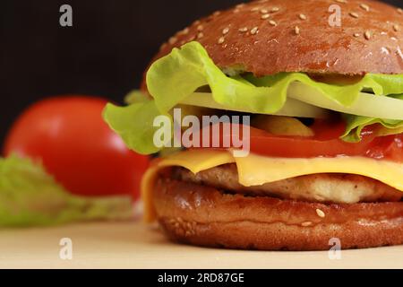 Cheeseburger avec côtelette de poulet gros plan. Hamburger maison et tomates à proximité. Restauration rapide. Banque D'Images