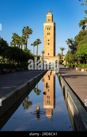 Ancienne tour minaret de la mosquée Koutoubia, site du patrimoine mondial de l'UNESCO, reflétée dans l'eau dans un parc bordé de palmiers, Marrakech, Maroc Banque D'Images