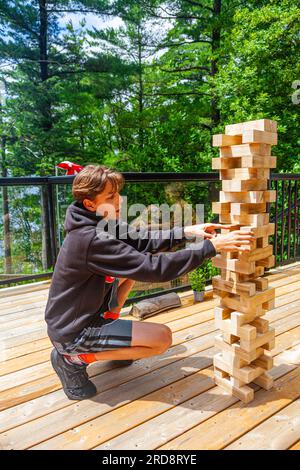 Garçon adolescent jouant avec une grande tour Jenga dans un chalet au bord du lac à Muskoka Ontario Canada Banque D'Images