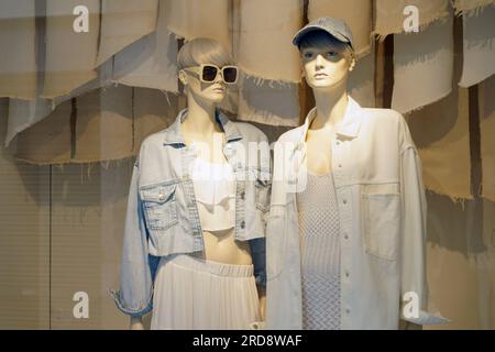 Vitrine d'une boutique vendant des vêtements pour femmes. Derrière le verre se trouvent deux mannequins féminins vêtus d'une jupe, d'une veste, de lunettes et d'autres vêtements. L'ima Banque D'Images