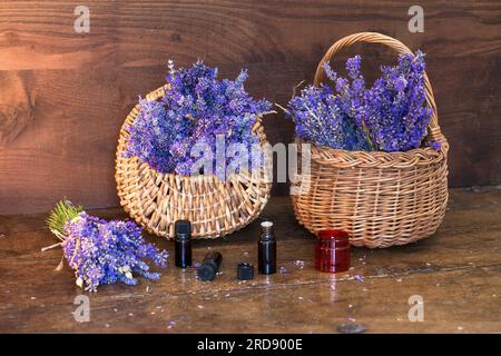 Lavande fraîche (Lavandula angustifolia) dans des paniers en osier et bouteilles d'huile essentielle sur une table en bois Banque D'Images