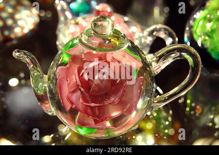 Beautiful glistening teapot replica has blown glass features and pink rose encased inside. Stock Photo