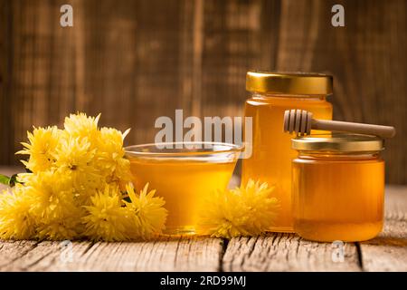 Composition créative de miel dans un bocal en verre et un bol, un godet en bois et des fleurs jaunes sur un fond en bois vieilli Banque D'Images