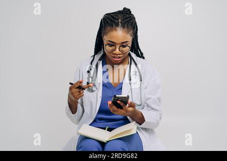Portrait d'un médecin afro-américain ou d'une femme infirmière portant une blouse de laboratoire tenant le smartphone sur fond blanc Banque D'Images