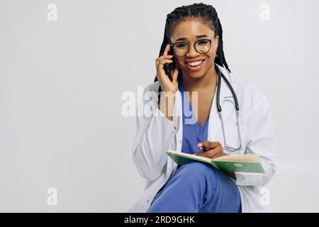 Portrait d'un médecin afro-américain ou d'une femme infirmière portant une blouse de laboratoire tenant le smartphone sur fond blanc Banque D'Images