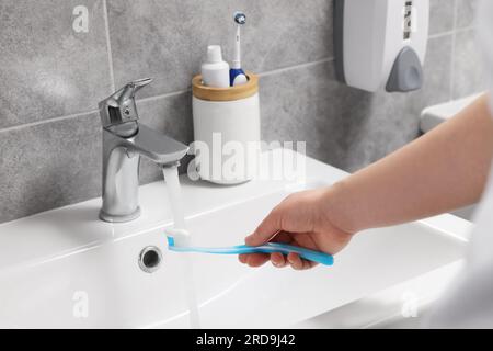 Femme lavant la brosse à dents en plastique sous l'eau qui coule du robinet dans la salle de bain, closeup Banque D'Images