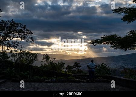 Tegucigalpa, Francisco Morazan, Honduras - 11 décembre 2022 : Femme regardant une vue panoramique de la ville de Tegucigalpa avec des arbres et des rayons de lumière à Sunse Banque D'Images