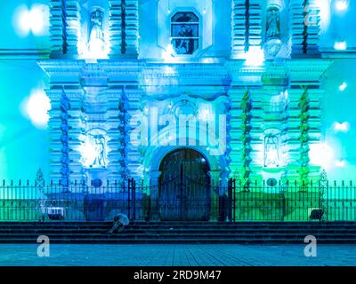 Tegucigalpa, Francisco Morazan, Honduras - 11 décembre 2022 : façade principale de la cathédrale de Tegucigalpa la nuit éclairée par des lumières bleues et vertes avec sommeil de femme Banque D'Images