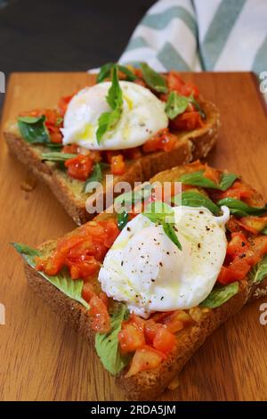 Délicieuse paire de toasts avec œuf poché sur tomates fraîches et feuilles de basilic Banque D'Images