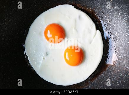 Vue de dessus de la paire de côté ensoleillé vers le haut oeufs étant frits dans une casserole Banque D'Images