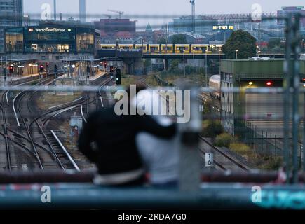 Berlin, Allemagne. 20 juillet 2023. Un couple s'assoit sur le pont Mordersohn tôt le matin avec pour toile de fond les voies ferrées. En arrière-plan, un tramway traverse le pont de Varsovie. Le pont est un lieu de rencontre populaire pour les habitants et les touristes. Crédit : Soeren Stache/dpa/Alamy Live News Banque D'Images